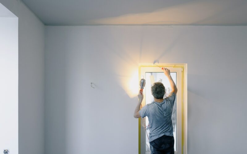 A man holding a light and finishing the paint job on his home's walls.