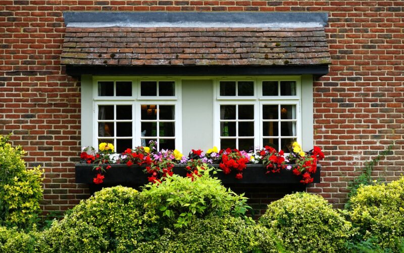 A home's outside windowsill covered in colorful flowers and shrubbery.