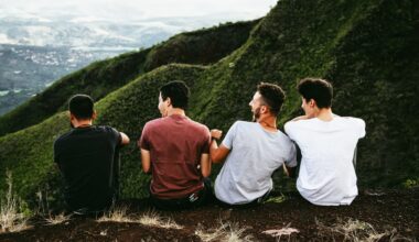 four guys sitting on top of a hill laughing and looking down