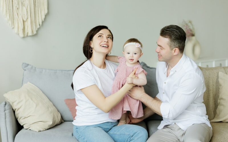 A man, woman, and baby sitting on the couch smiling
